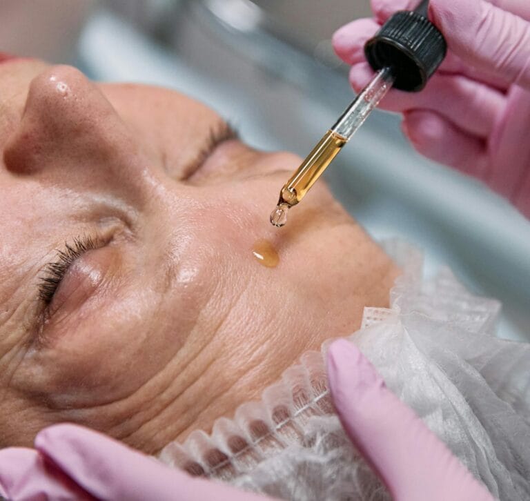 Senior woman receiving a facial serum treatment in a spa setting.